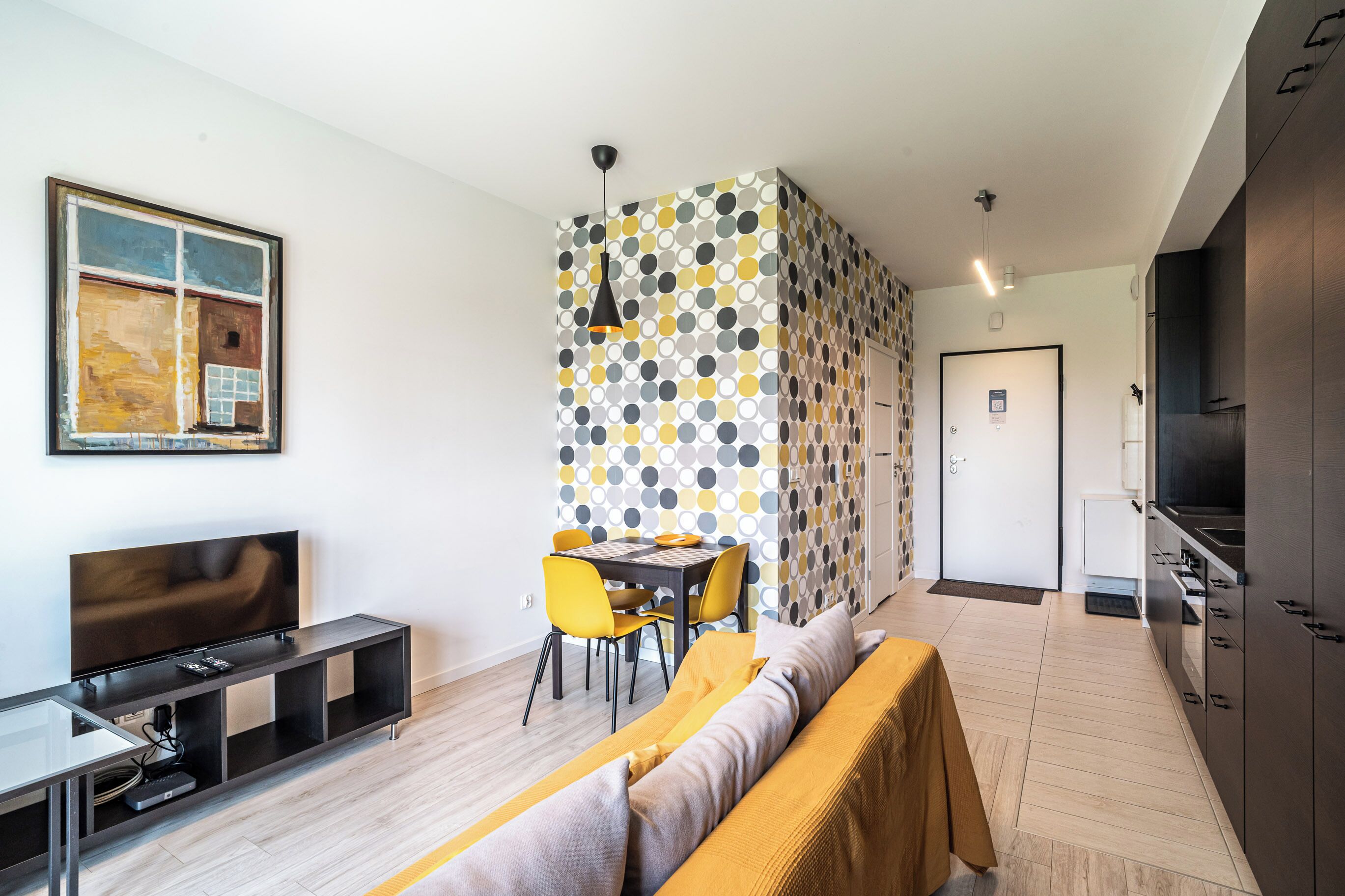 A modern living space with a dining area, a sofa, a TV, and a kitchen.