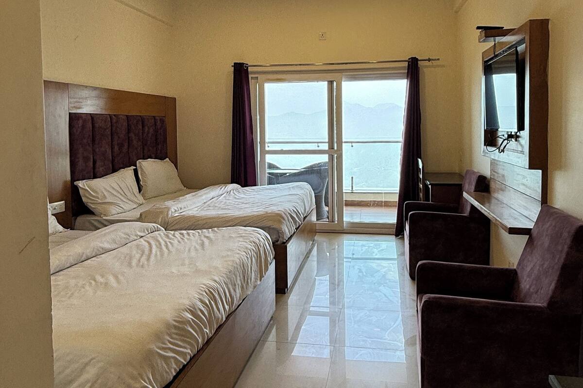 A hotel room with two beds, a TV, a seating area, and a view of the sea.