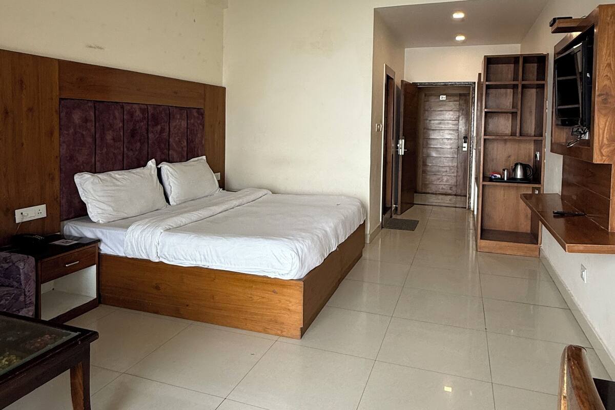 A bedroom with a wooden bed, a nightstand, a desk, a chair, and a TV.