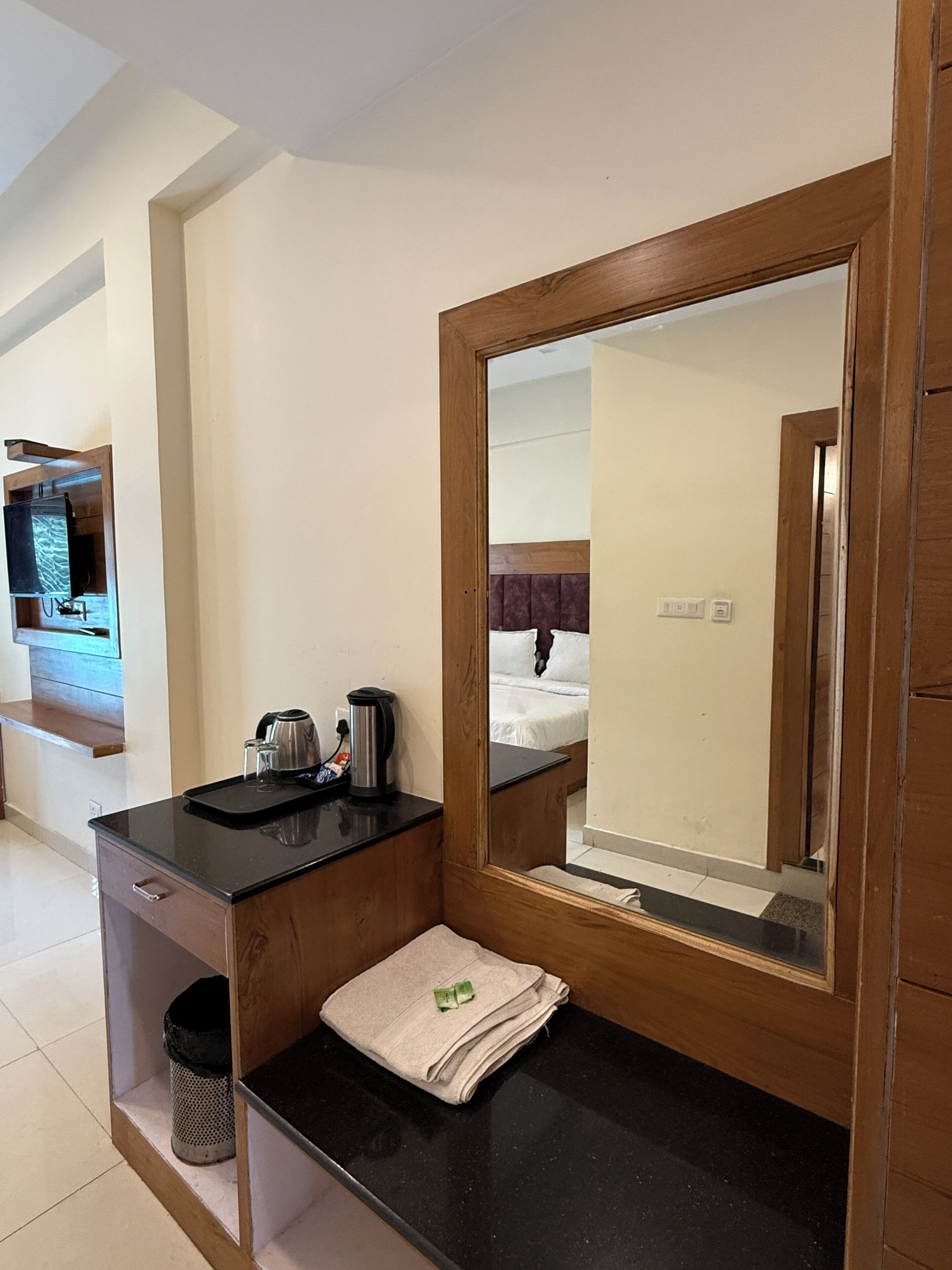 A hotel room with a wooden vanity, a mirror, a bed with a purple headboard, and a television on a wooden shelf.