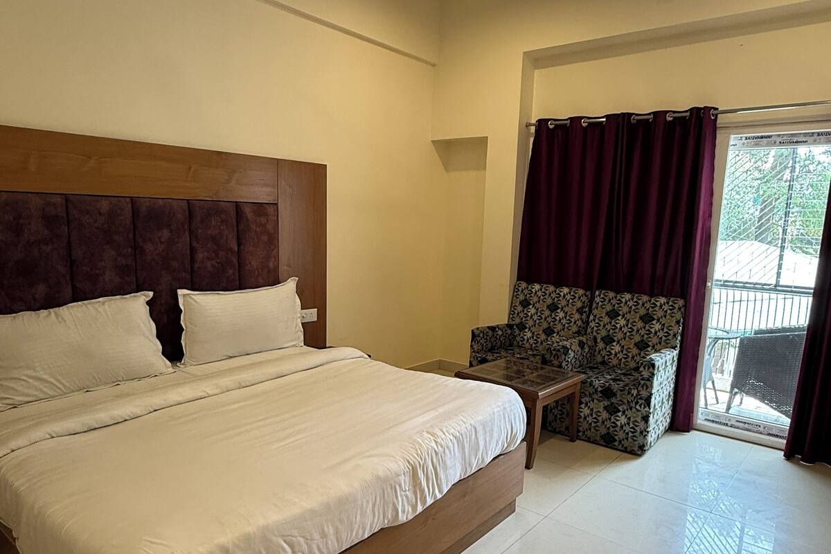 A hotel room with a large bed, a ceiling fan, a window with curtains, and a small table with a chair.