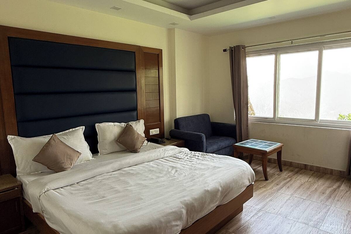 A hotel room with a large bed, a ceiling fan, a window with curtains, and a small table.