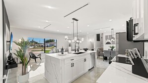 A modern kitchen with a central island, white cabinetry, and a large window offering a view of the outdoors. - Modern 5BR Dream • Courts, Playground • Pool_BBQ (Miami)