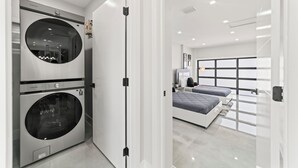 A modern bedroom with a large bed, a built-in washing machine, and a large window. - Modern 5BR Dream • Courts, Playground • Pool_BBQ (Miami)