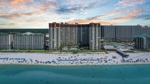 Un hotel frente a la playa con varios edificios altos, una playa de arena y un área de piscina.