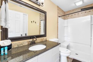 Ein Badezimmer mit Granitwaschtisch, Toilette in Weiß, großem Spiegel und Duschbereich.