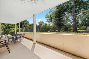 Eine Terrasse im Freien mit Tisch und Stühlen, einem Deckenventilator und einem Maschendrahtzaun.