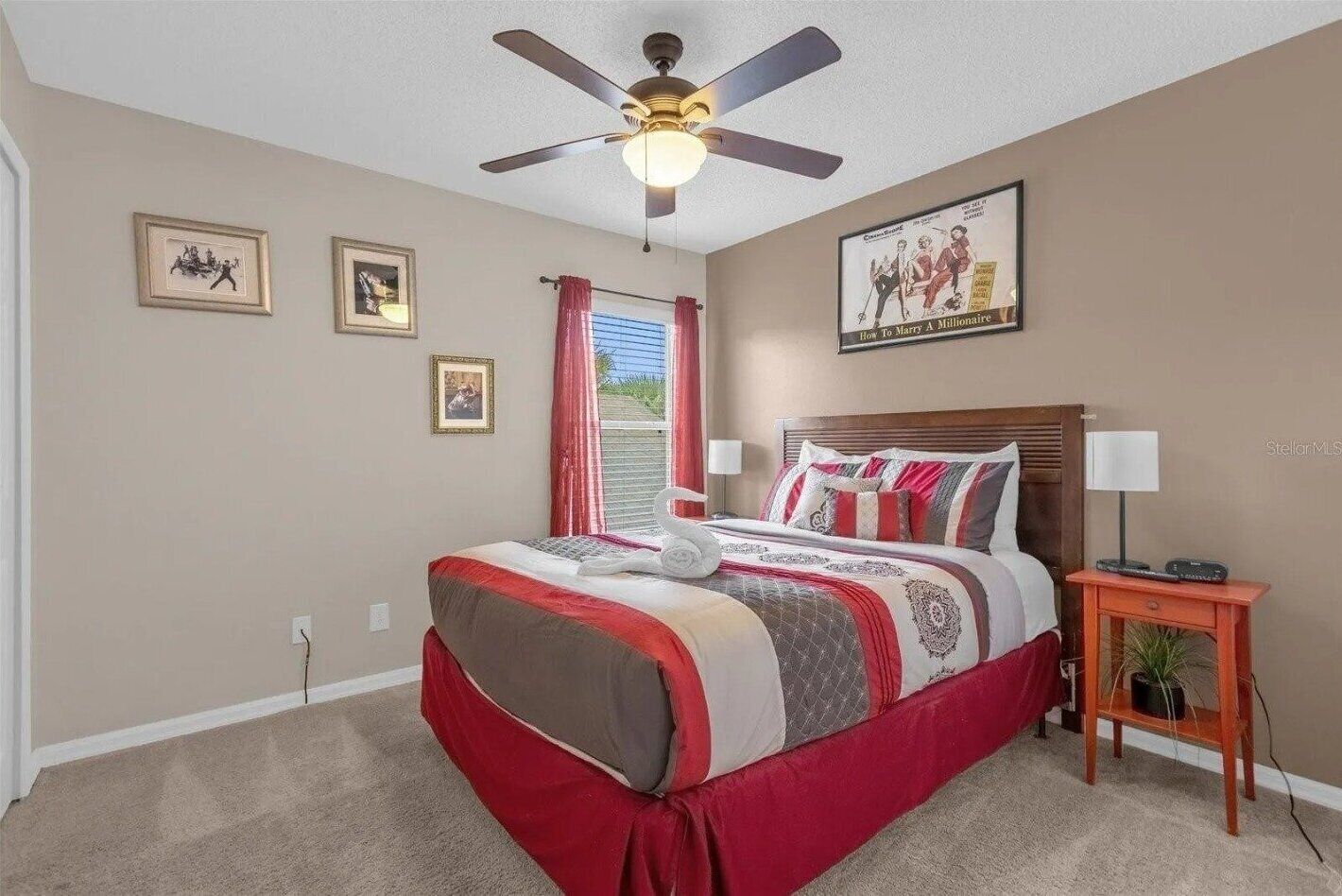 A bedroom with a bed, a ceiling fan, a nightstand with a lamp, and a framed picture on the wall.
