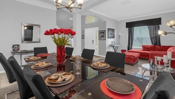 Un espace de repas moderne agrémenté d’un lustre, d’un vase rouge contenant des fleurs et d’un canapé rouge dans le salon.