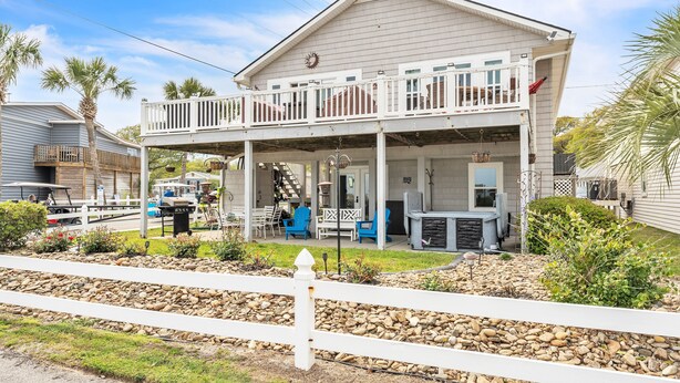 A two-story house with a balcony, a patio with outdoor furniture, and a stone pathway. - Coastal Camelot - Walk To Surfside Beach 2 Bedroom Duplex (Murrells Inlet)