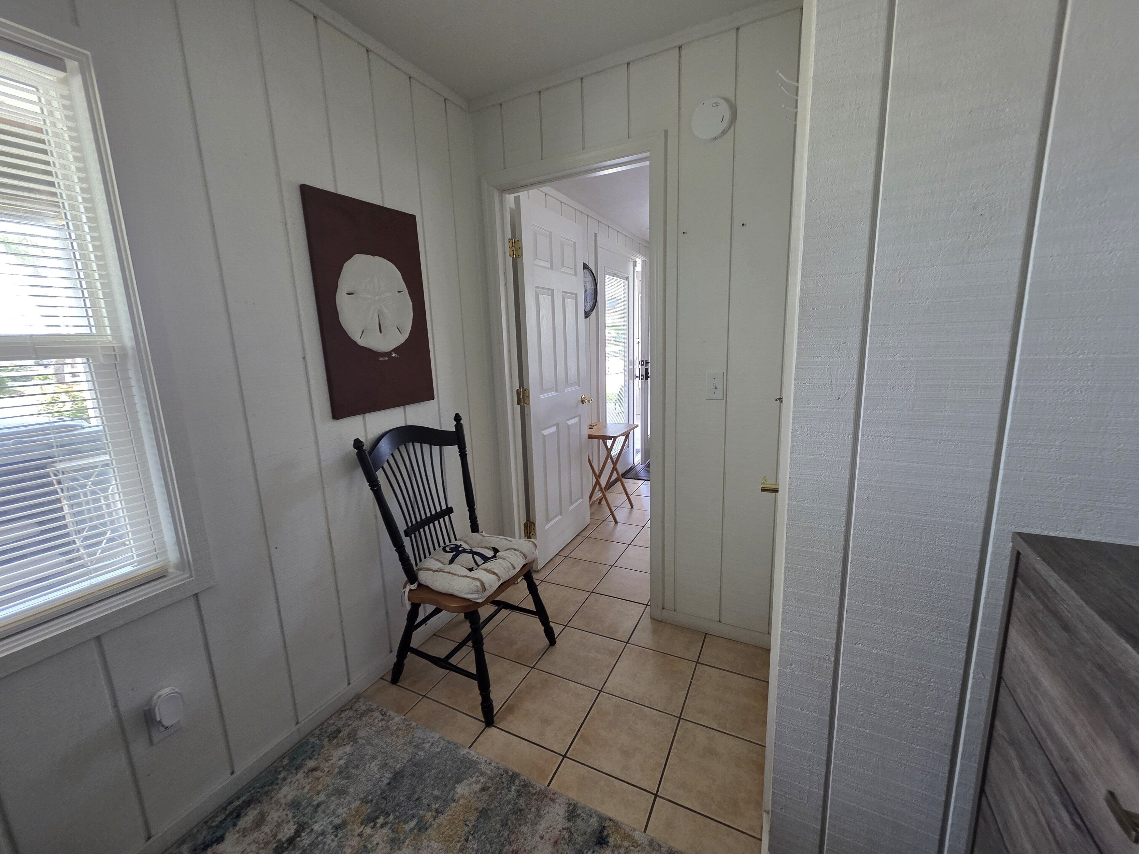 A hallway with a chair, a clock, and a door leading to another room.