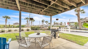 An outdoor patio with a round table and chairs, a grill, and hanging baskets. - Coastal Camelot - Walk To Surfside Beach 2 Bedroom Duplex (Murrells Inlet)