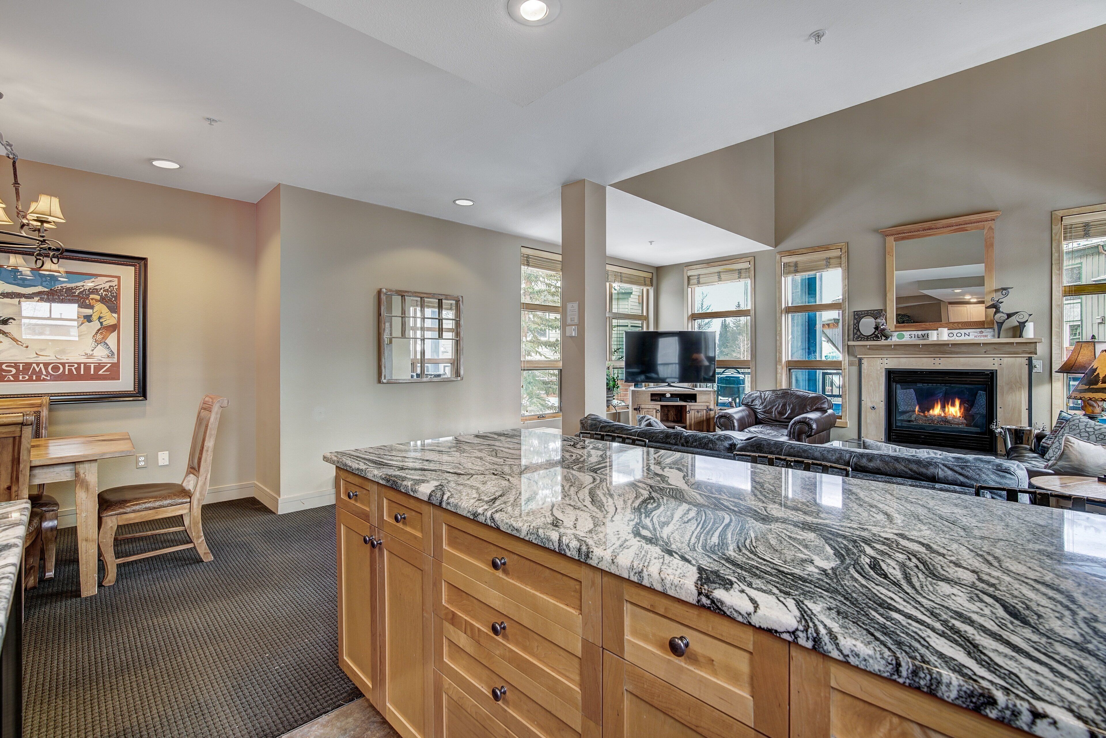 A spacious kitchen with a large marble island, wooden cabinets, and a built-in fireplace.