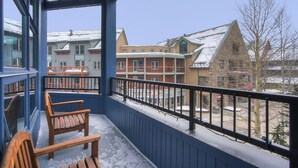 A balcony with wooden chairs, a snow-covered ground, and buildings in the background. - Fantastic Mountain Home Near Ski Lifts 3 Bedroom Condo (Keystone)