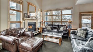A spacious living room with leather sofas, a fireplace, large windows, and a view of the outside. - Fantastic Mountain Home Near Ski Lifts 3 Bedroom Condo (Keystone)