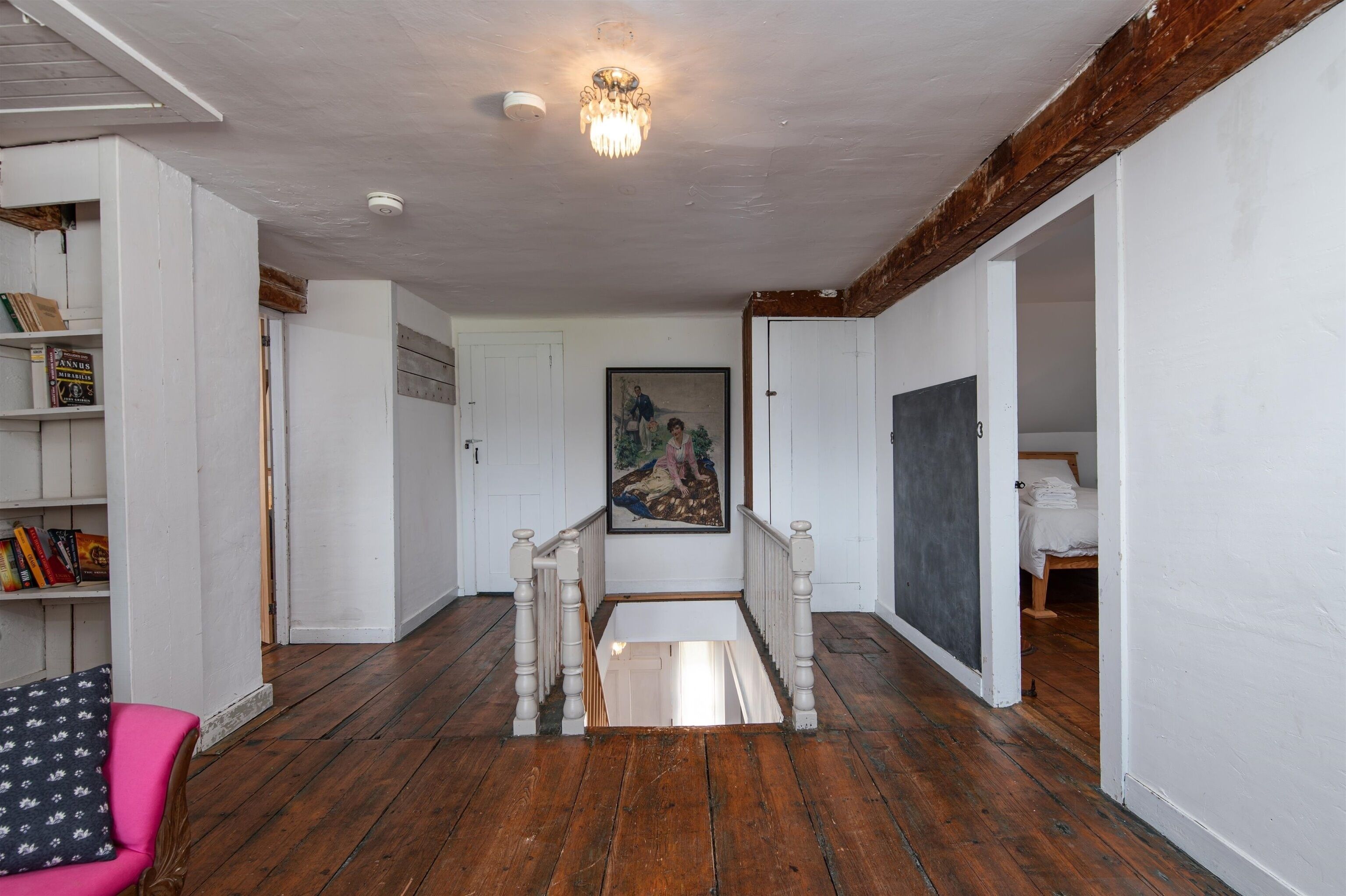 A hallway with wooden flooring, white walls, a chandelier, a staircase, and a painting on the wall.