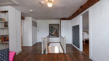 A hallway with wooden flooring, white walls, a chandelier, a staircase, and a painting on the wall.