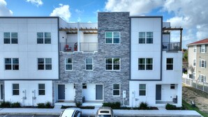 Un immeuble résidentiel moderne à plusieurs étages, doté d’une façade en pierre, de nombreux balcons et d’un espace de stationnement à l’avant.