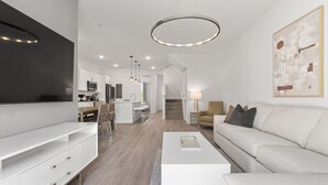 Un salon moderne avec un canapé blanc, une table basse et un téléviseur à écran plat fixé au mur. Il y a également un coin cuisine avec un four à micro-ondes et un espace repas avec des chaises.