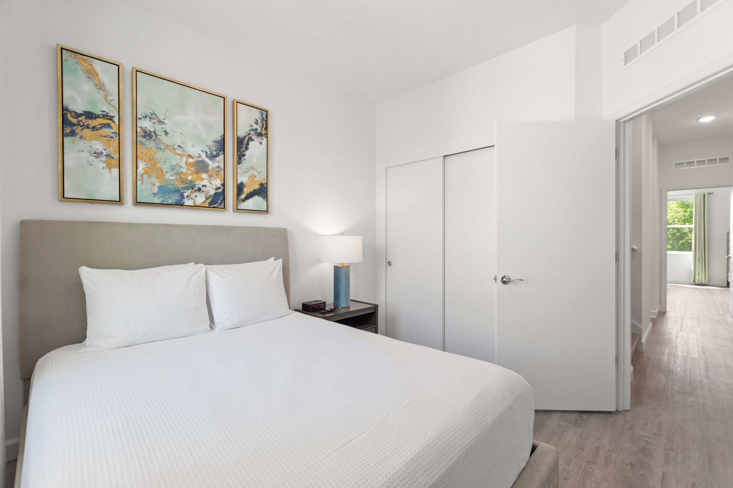 A modern hotel room with a large bed, a nightstand with a lamp, and abstract art on the wall.
