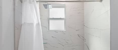 A bathroom with a shower, a window, and a bathtub.