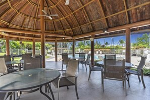 Un espacio al aire libre cubierto con mesas y sillas, una piscina y vistas a la vegetación circundante.
