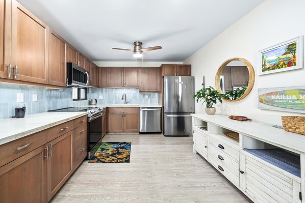 Una cocina moderna con armarios de madera, electrodomésticos de acero inoxidable, un ventilador de techo y un espejo decorativo.