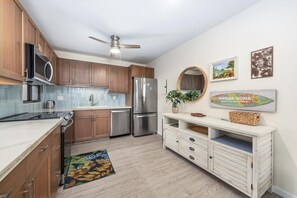 A modern kitchen with wooden cabinets, stainless steel appliances, a ceiling fan, and decorative wall art.