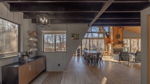 A spacious kitchen with wooden cabinets, a dining area with a table and chairs, and a view of the outdoors through large windows. - Whitetail Creek Retreat by Innsbrook Vacations! (Innsbrook)
