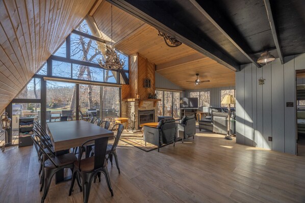 A spacious interior with a dining area, seating, a fireplace, and large windows offering views of the outdoors.
