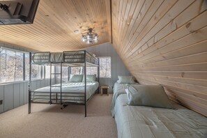 A bunk bed room with a wooden ceiling, a small stool, and a window with blinds.