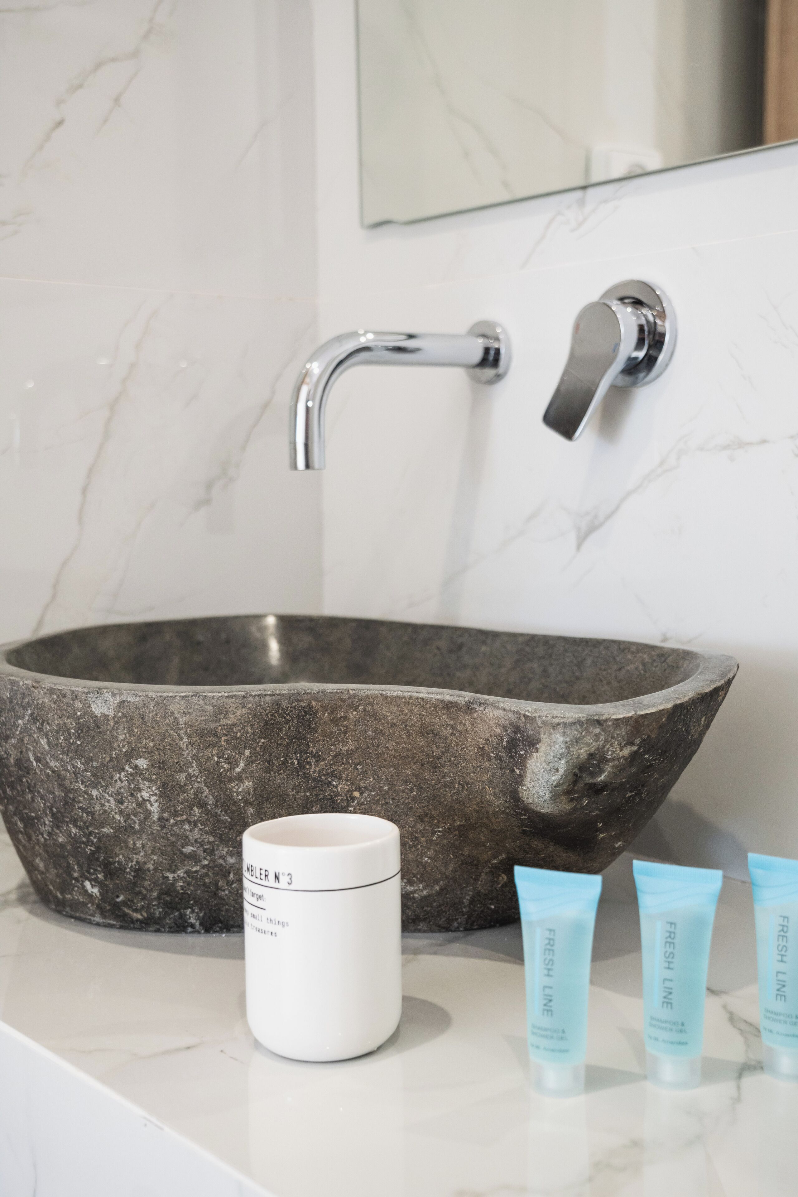 Un baño con un lavamanos grande de piedra oscura, una taza de cerámica blanca y tres tubos azules de productos Fresh Line.