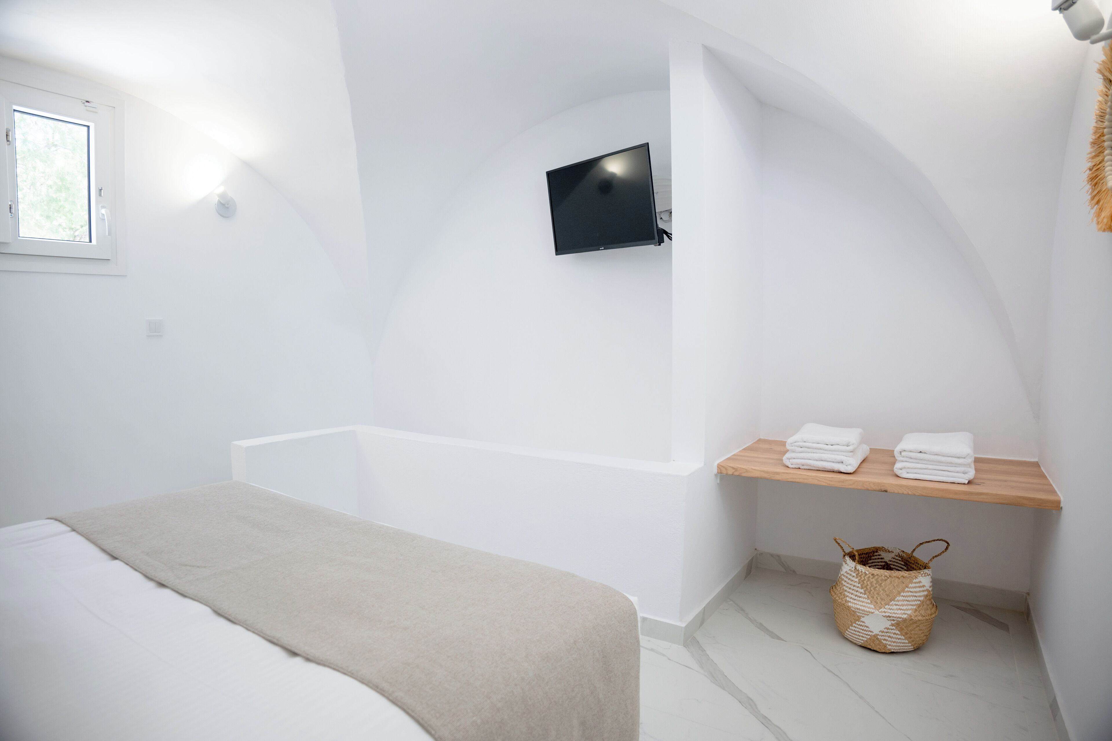 A modern bathroom with a bathtub, a mounted TV, and a shelf with towels.