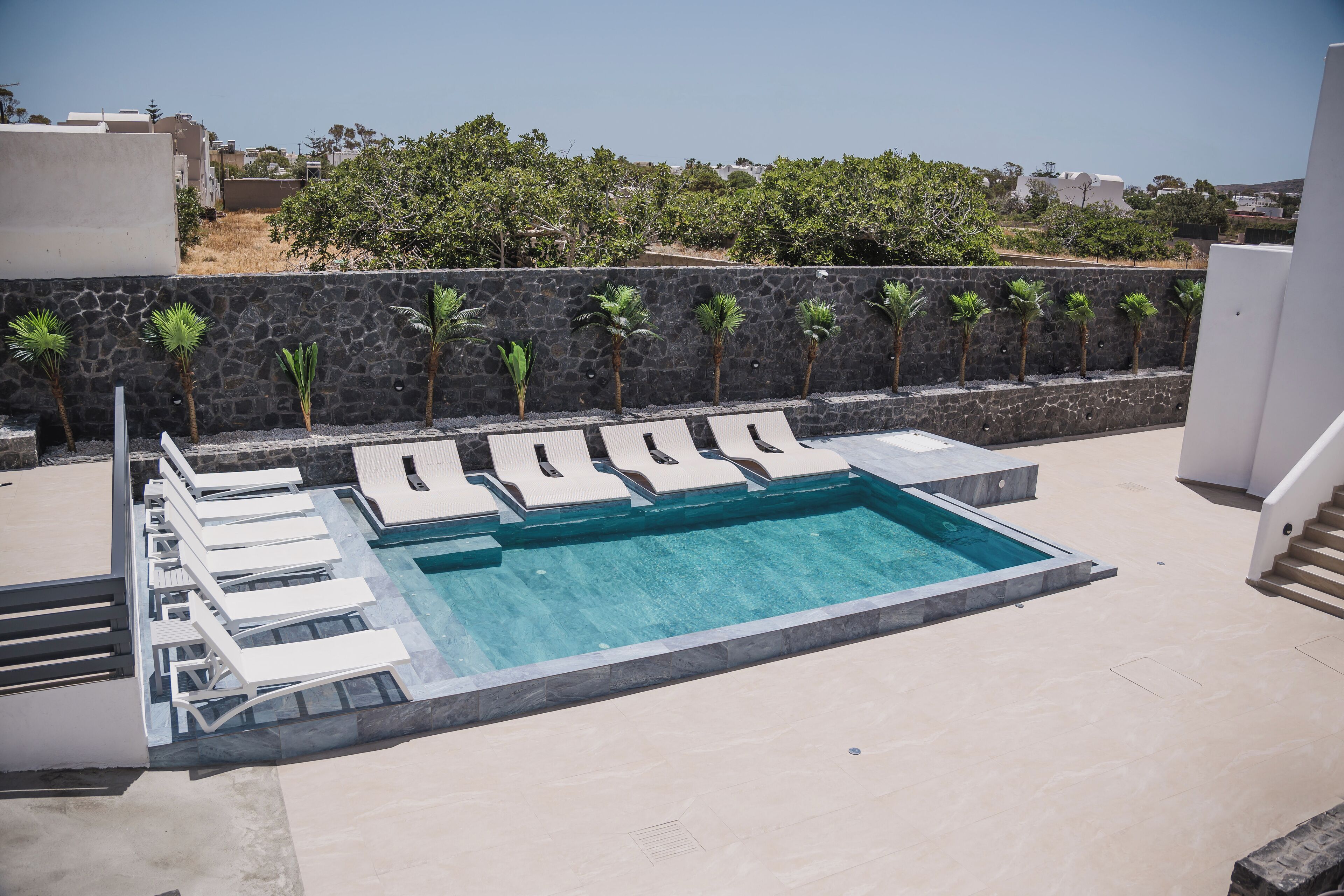 A rooftop pool area with lounge chairs and a stone wall with palm trees.