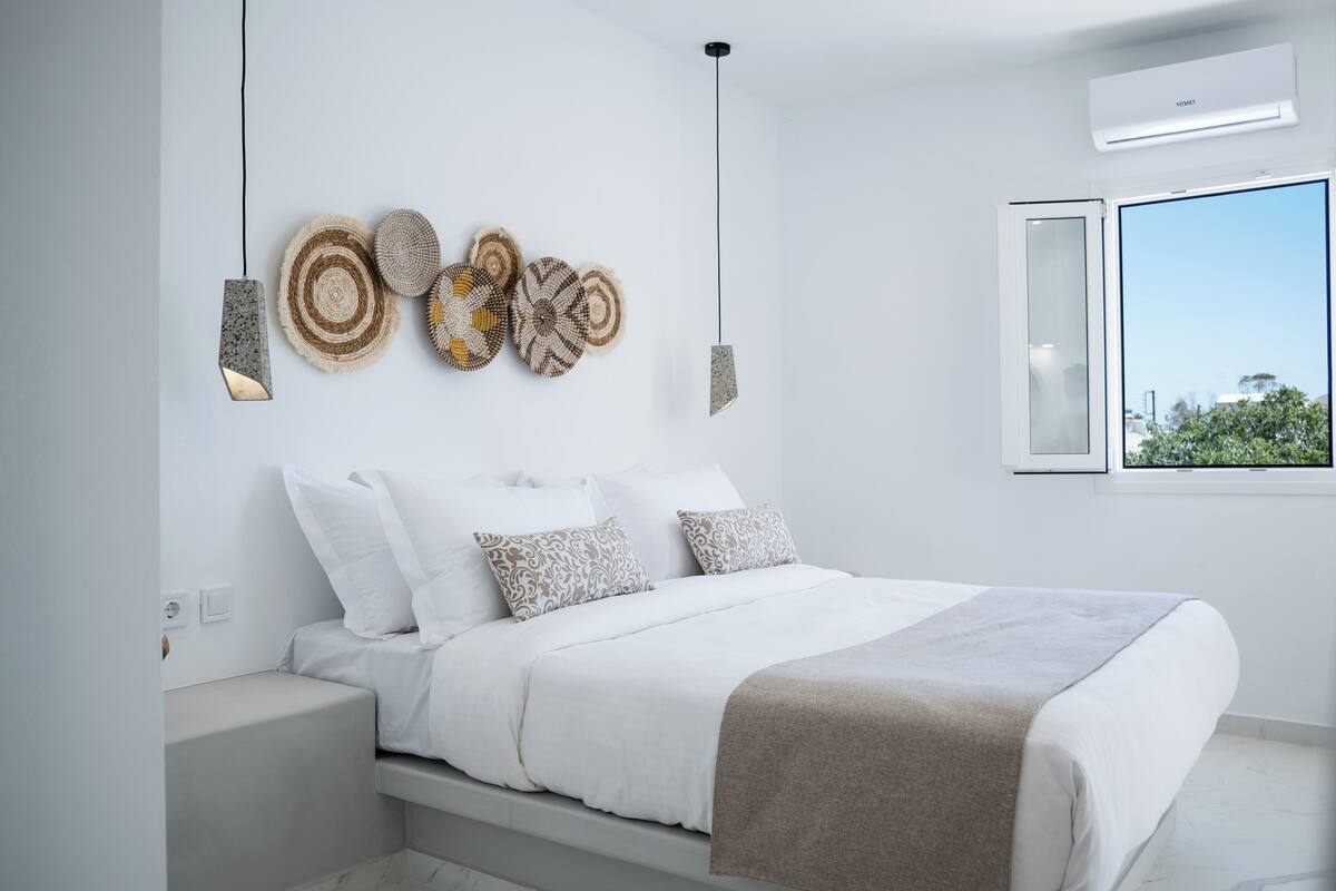 Un dormitorio moderno con cama, ropa de cama blanca, decoración en la pared y ventana con vistas.