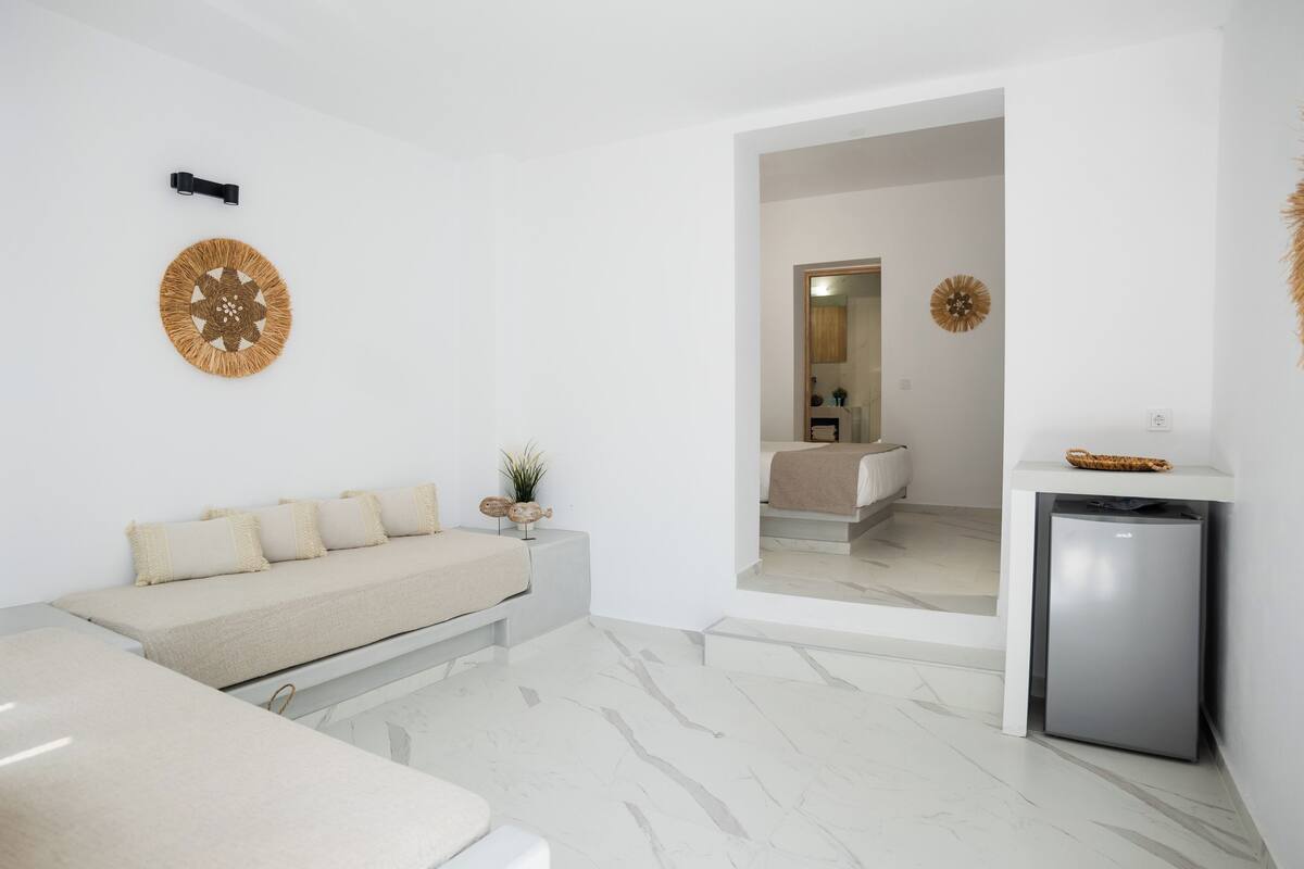 Un dormitorio moderno y minimalista con cama, mesita de noche y un refrigerador pequeño.