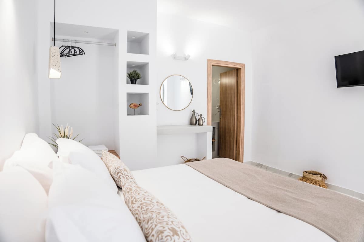 Un dormitorio moderno con una cama grande, una mesita de noche, un espejo y un televisor en la pared.