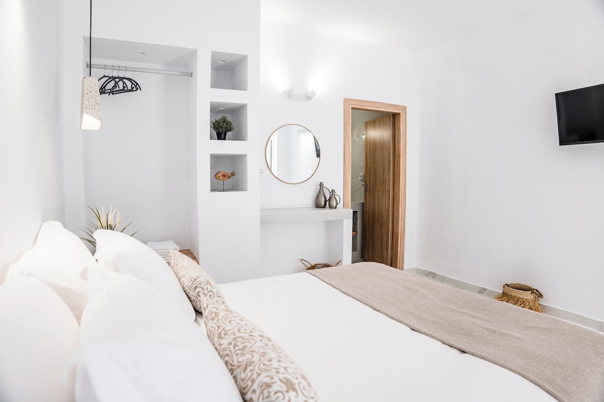 A modern bedroom with a large bed, a bedside table, a mirror, and a TV mounted on the wall.