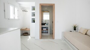 Un dormitorio moderno con una cama grande, una puerta de madera que da a un baño y una pared blanca con una ventana y estanterías.