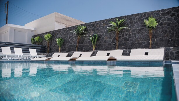 Una piscina con sillas de descanso blancas y palmeras frente a una pared de piedra.