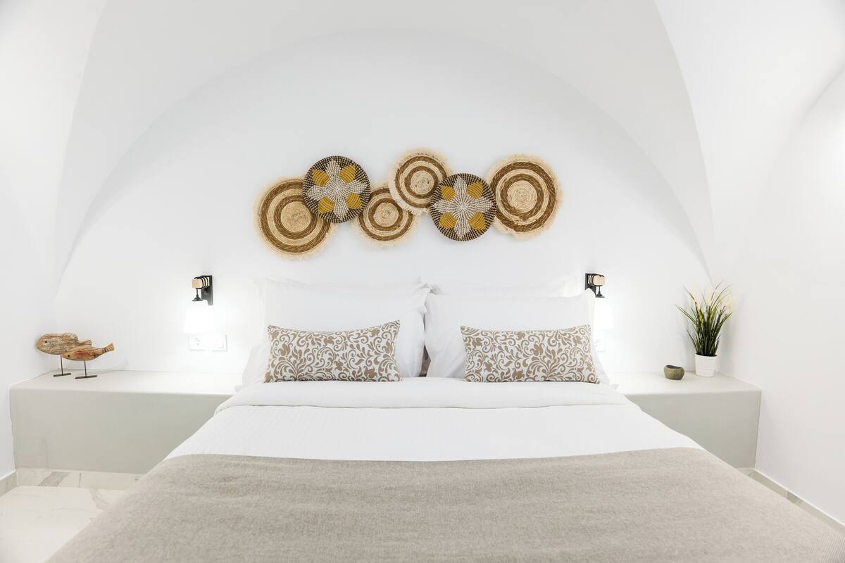 Un dormitorio moderno con una cama grande, dos mesitas de noche, un adorno de pared y una planta pequeña.
