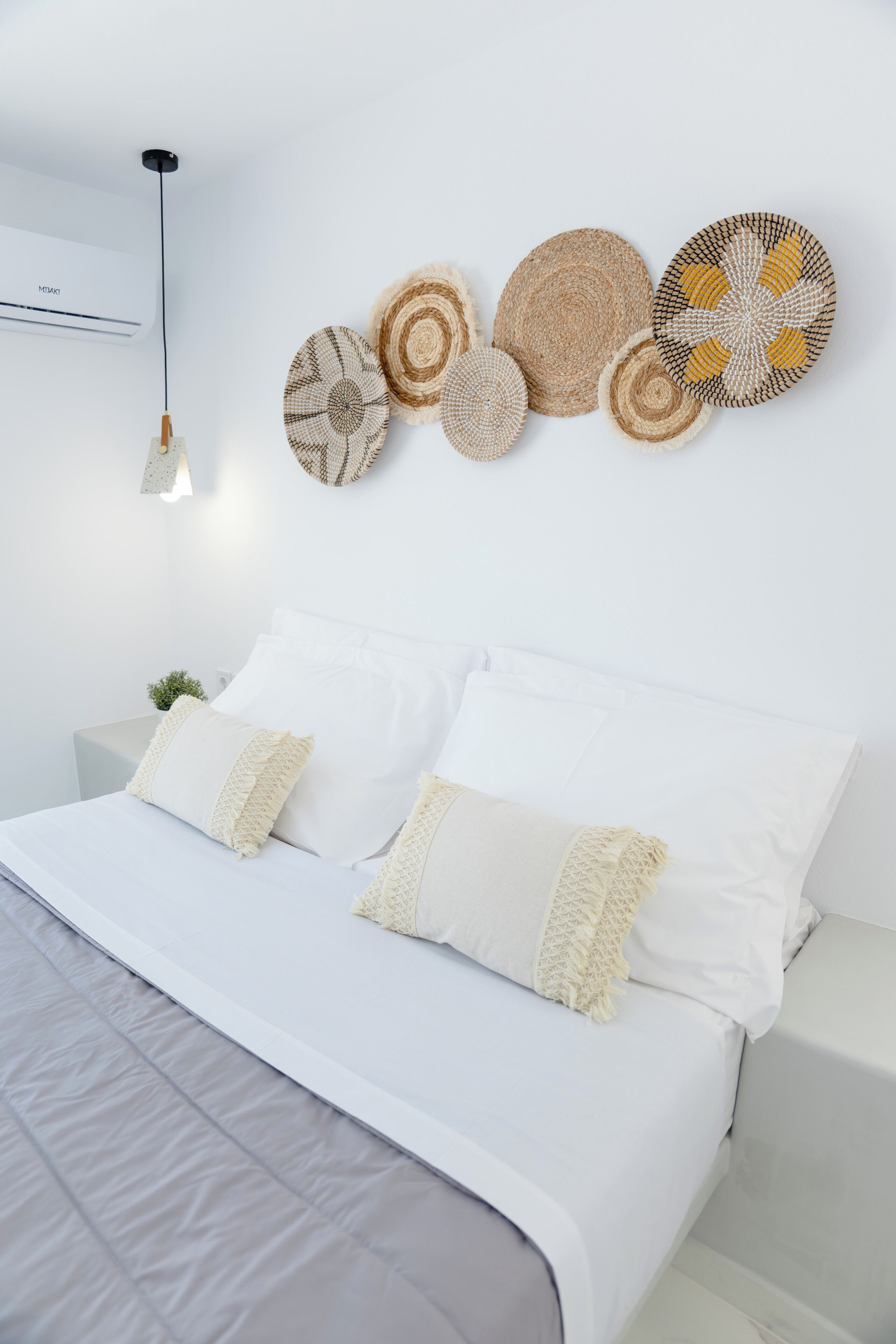 A modern bedroom with a bed, white bedding, and a wall-mounted air conditioner.