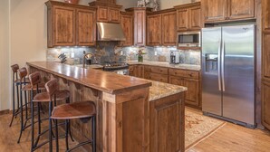 Una cocina con armarios de madera, un refrigerador de acero inoxidable, una barra con taburetes y un respaldo de piedra.