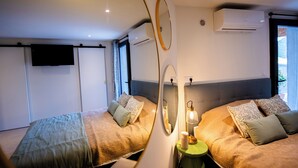 A modern hotel room with two beds, a flat-screen TV, a mirror, and a bedside table with a lamp. - 2-person apartment in Conca: Corsican paradise for rent between land and sea (Conca)