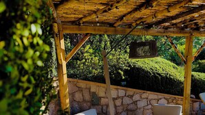 An outdoor patio area with stone flooring, a wooden pergola, and seating arrangements including a sofa and two chairs. - 2-person apartment in Conca: Corsican paradise for rent between land and sea (Conca)