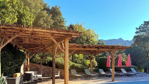 A poolside area with a pergola, lounge chairs, and umbrellas. - 2-person apartment in Conca: Corsican paradise for rent between land and sea (Conca)