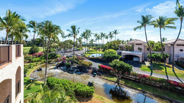 A resort with a landscaped garden, palm trees, a pond, and a building with a curved roof. - Includes Beach Gear!  332 Shores at Waikoloa (Waikoloa Beach Resort)