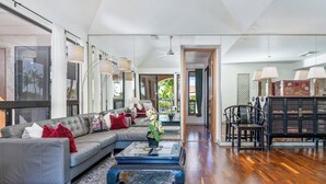 A spacious living room with a grey sectional sofa, a blue coffee table, and a patterned rug. There is a dining area with black chairs and a wooden table. - Includes Beach Gear!  332 Shores at Waikoloa (Waikoloa Beach Resort)