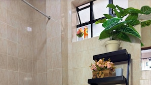 A modern bathroom with a toilet, a blue basin, a shelf with towels, a potted plant, and a window with flowers. - The Home Kololo (Kampala)