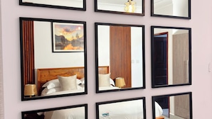 A wall with nine square mirrors of varying sizes, reflecting different parts of a room including a bed, a lamp, and a door. - The Home Kololo (Kampala)